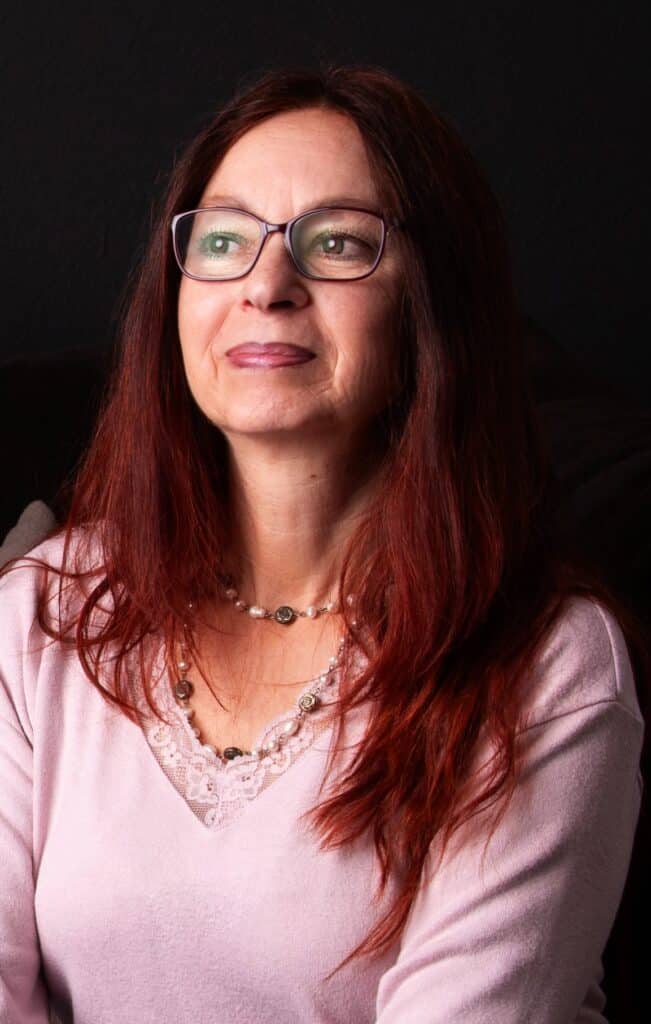 Babs mit rosa Pullover, nachdenklich und anthrazitfarbenem Hintergrund